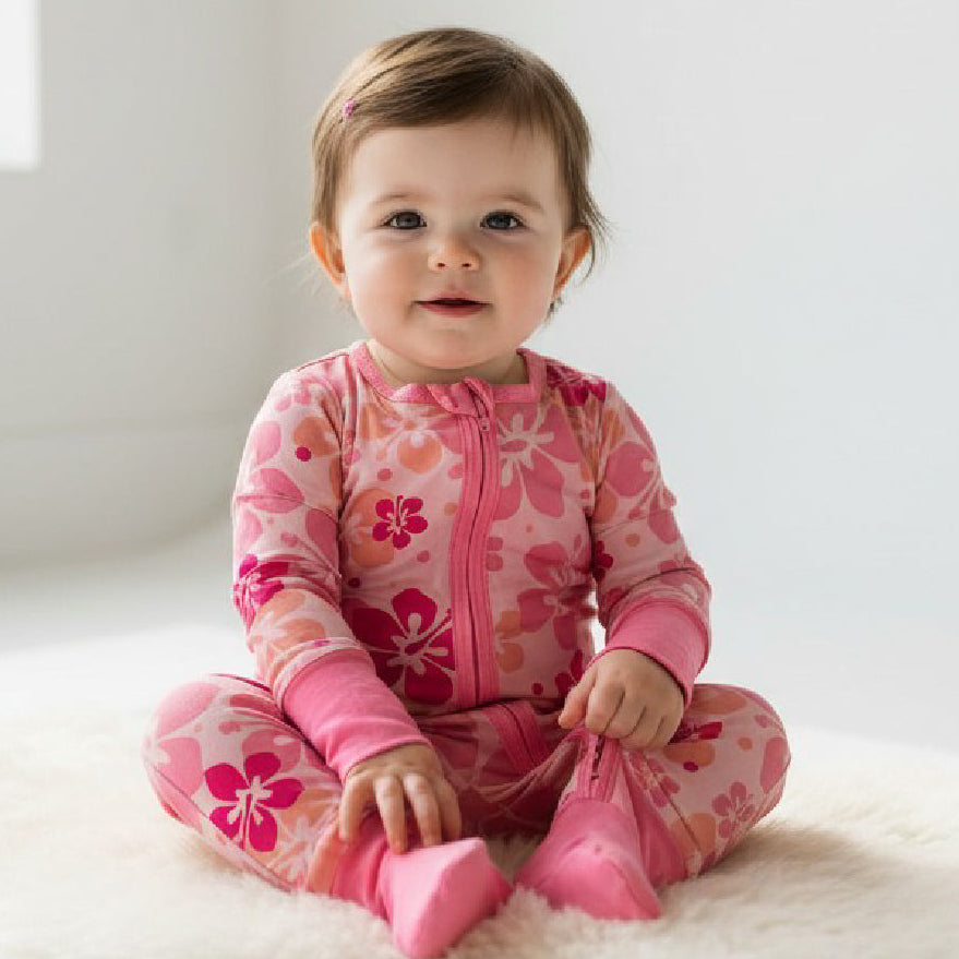 Baby wearing a pink floral outfit sitting on a white surface.