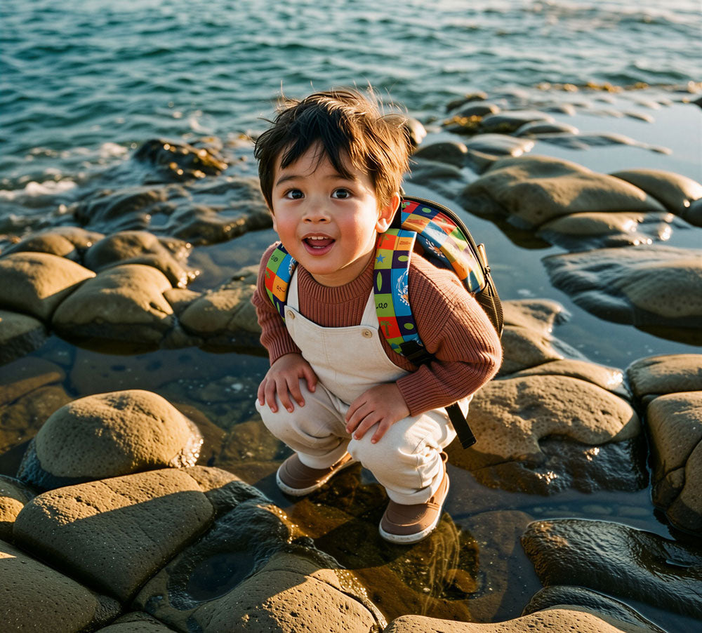 Image of Child playing on rocks by the water with a colorful backpack