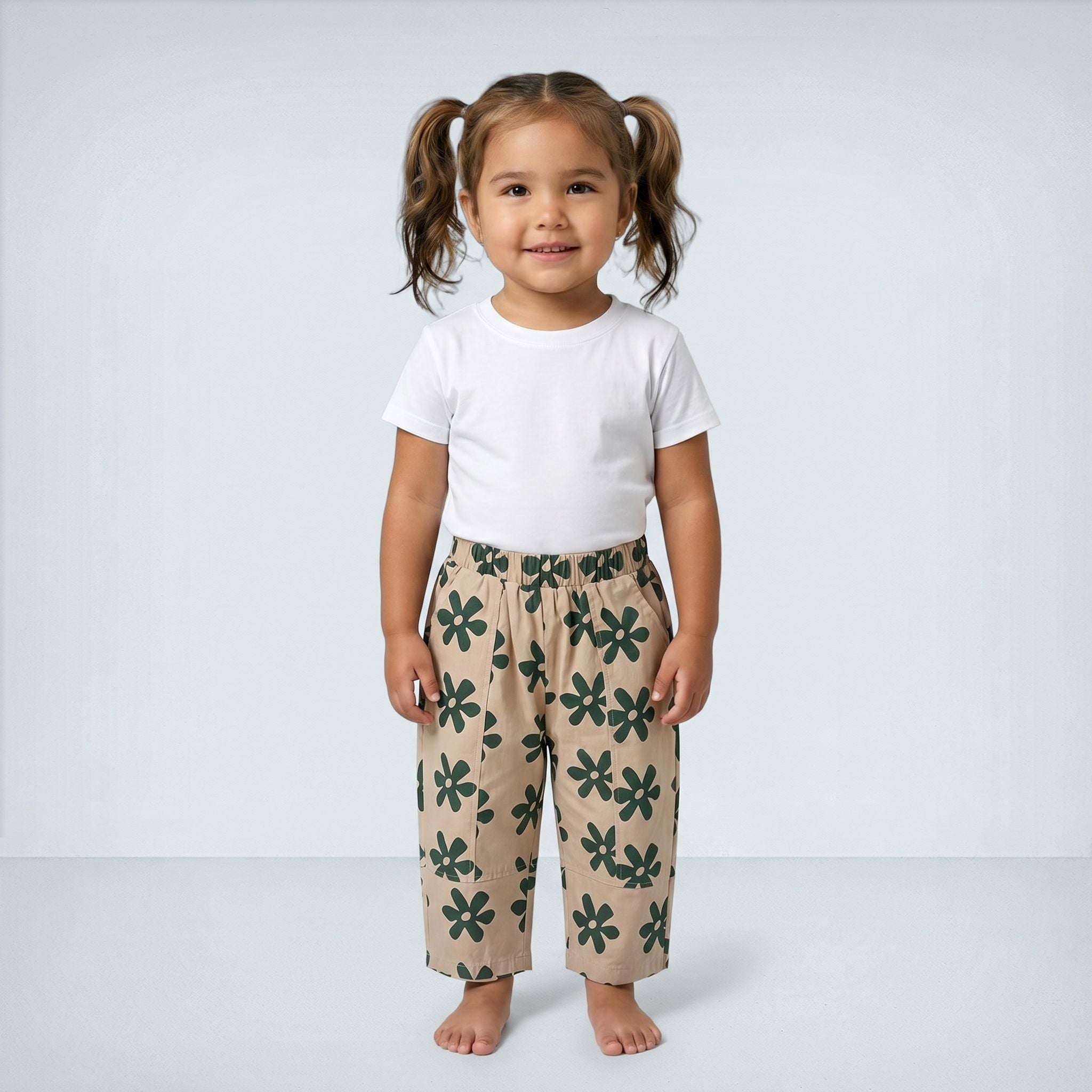 Child wearing a white t-shirt and beige pants with green floral pattern on a plain background