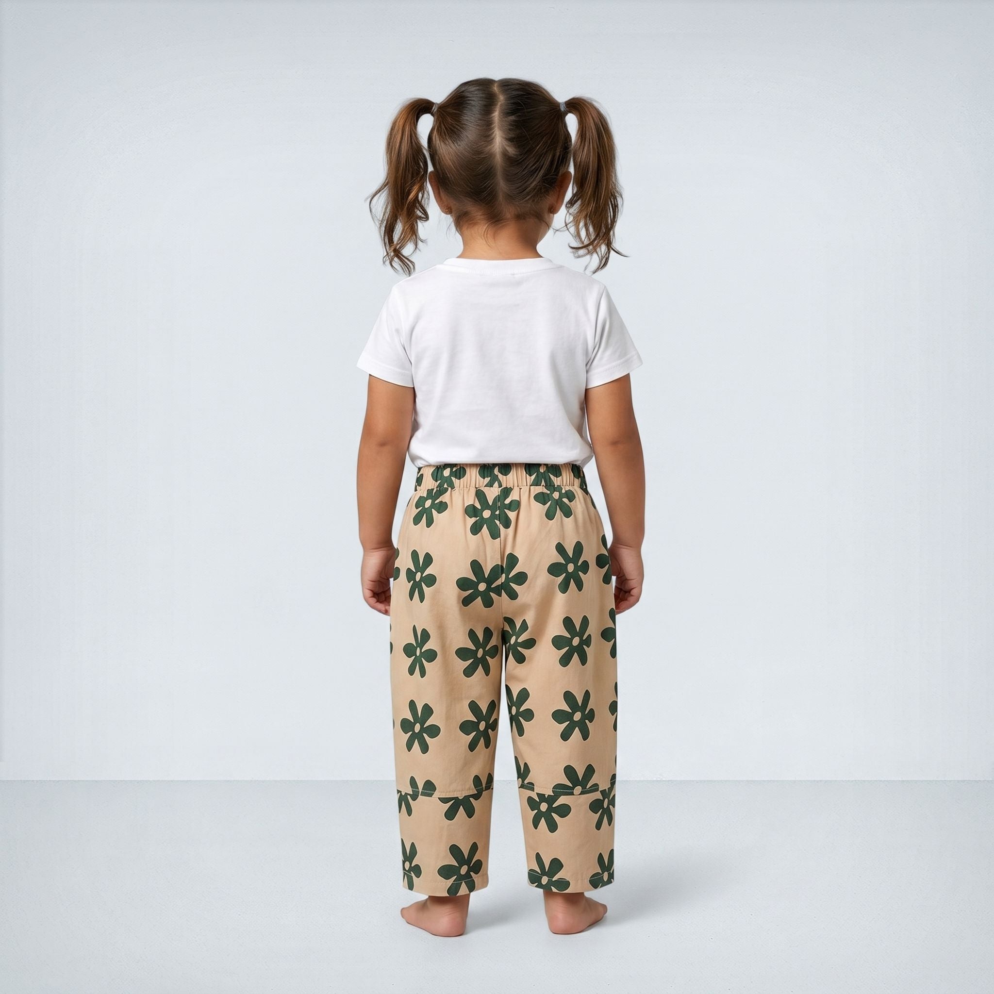 Child wearing a white shirt and beige pants with green floral pattern on a plain background